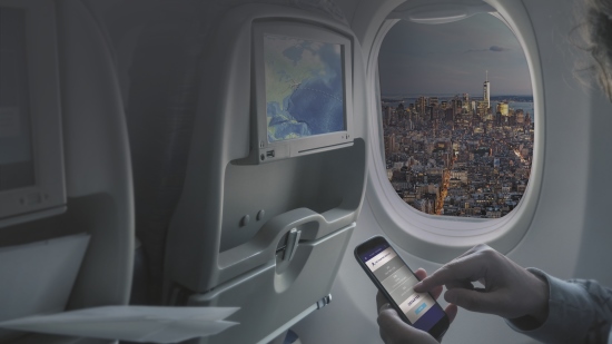 A person on their phone and TV onboard a plane with a city view out the window.